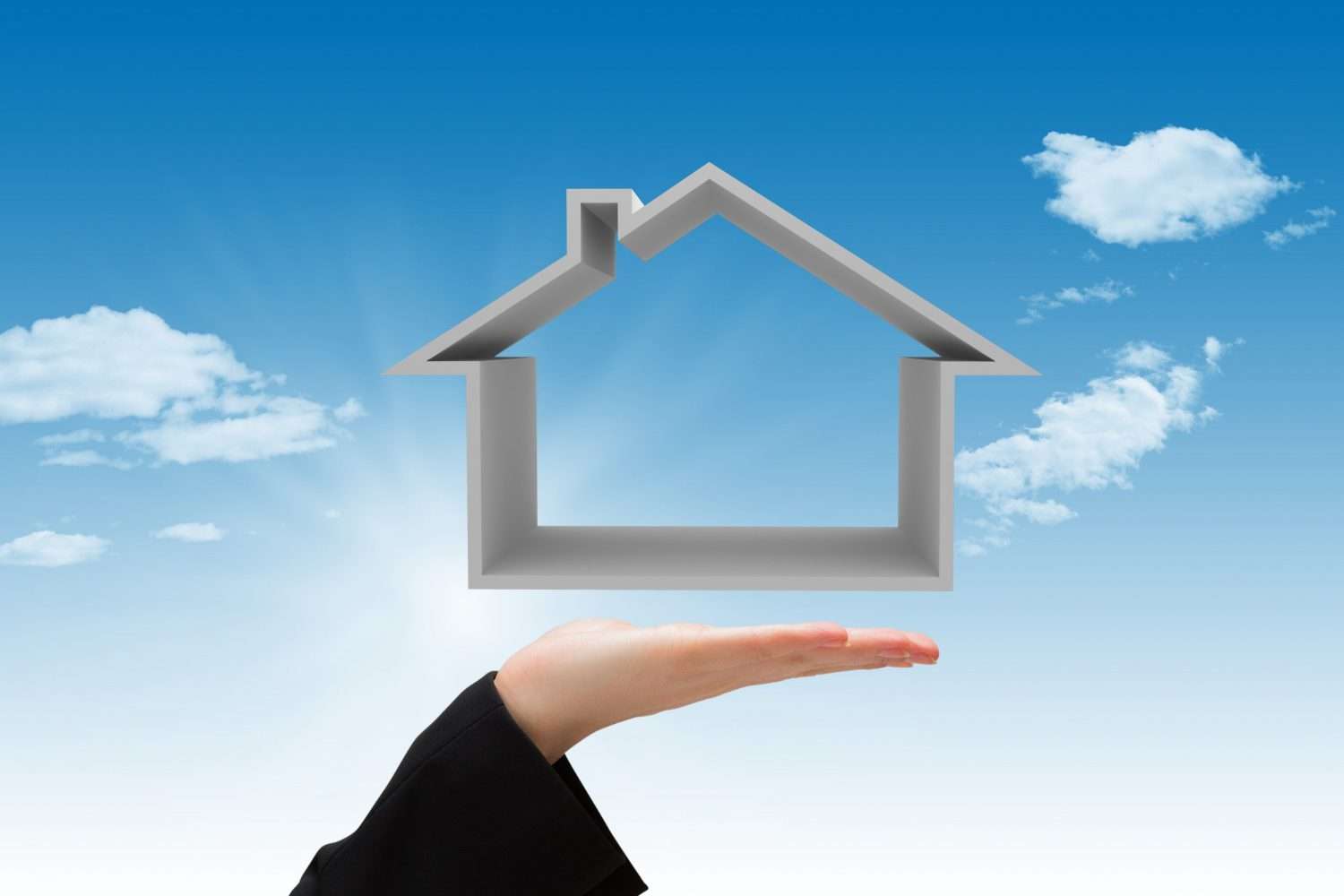 A hand holds a house-shaped outline against a blue sky with clouds.