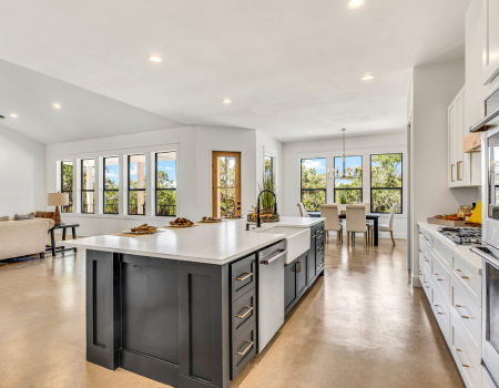 New Project - 2025-09-15T153106.787 Modern open-concept kitchen with a large island, white cabinets, stainless steel appliances, and adjacent dining and living areas with large windows.
